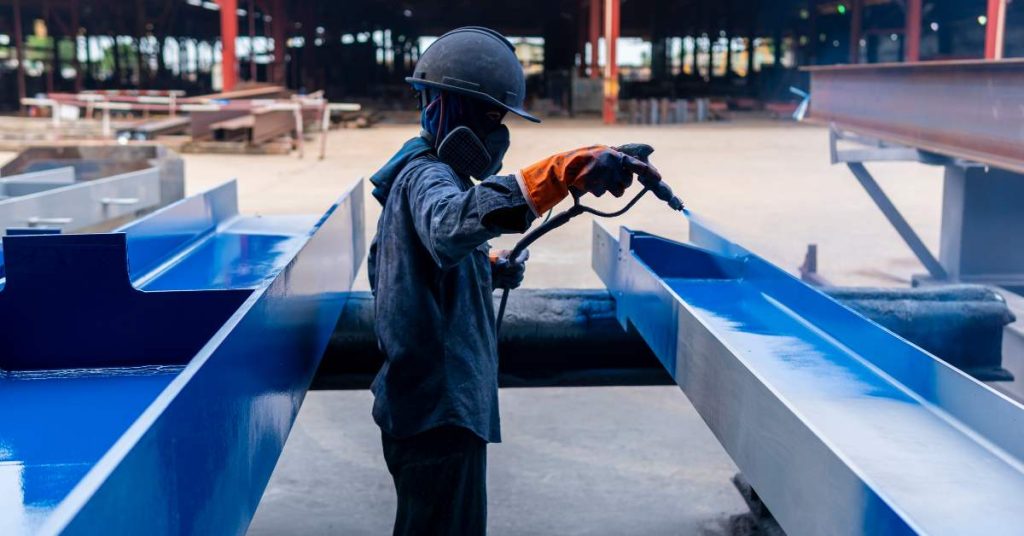 Professional spray painter applying blue coat over metal beams